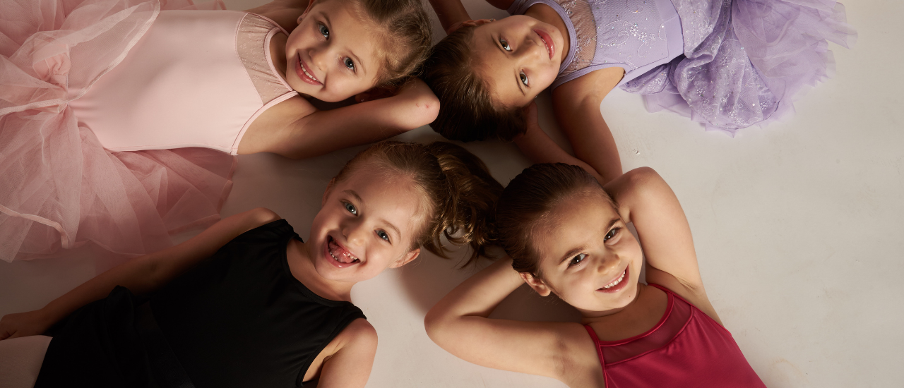 Young dancers pose for a photo laying in a circle