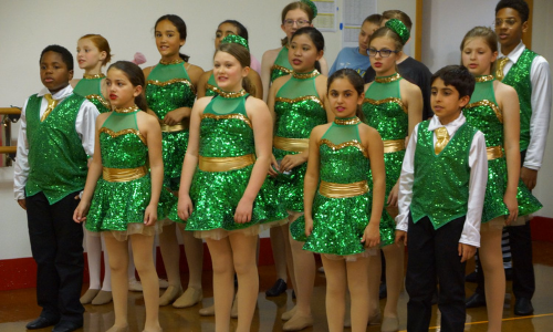 Dancers wearing green costumes prepare to perform