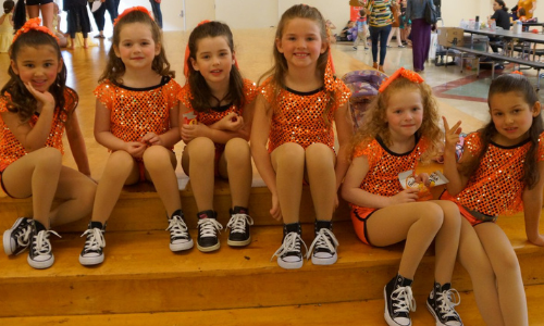Dancers wearing orange costumes prepare to perform